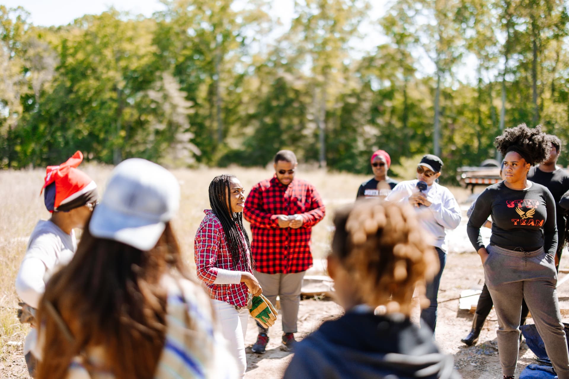Community members gathered outdoors on the farm listening to a speaker during a volunteer workday